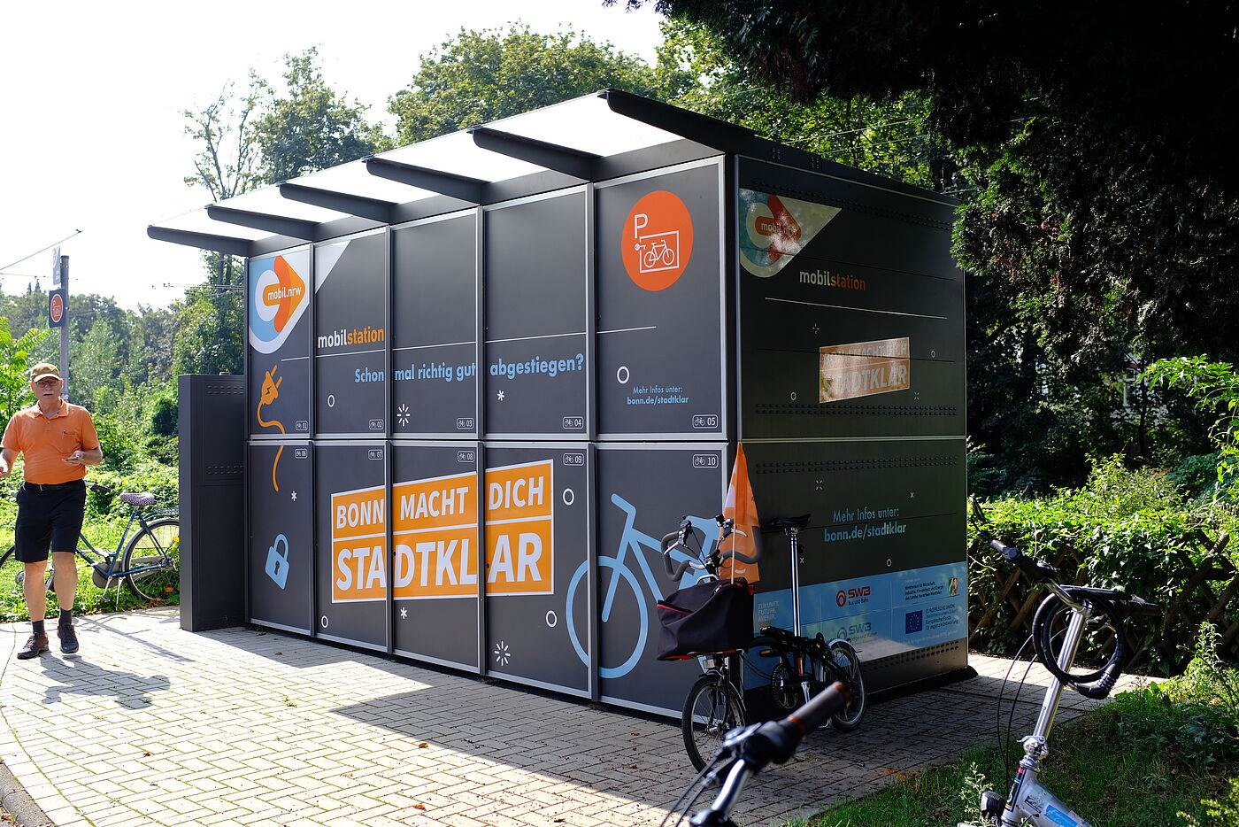 2024-08-Exkursion_Bonn_-_ADFC_NRW__9 Erste Station der Exkursion in Bonn war die Mobilstation in der Kaiserstraße. Gemeinsam mit den Bonner Stadtwerken errichtet die Stadt 30 Mobilstationen in der Innenstadt. Das Angebot der Mobilstationen umfasst u.a. verschließbare Fahrradboxen, überdachte Fahrradbügel, Verleih von Lastenrädern und Luftpumpen. Nicht alle Mobilstationen sind gleich – sie unterscheiden sich in Art und Zahl der vorhandenen Serviceangebote.