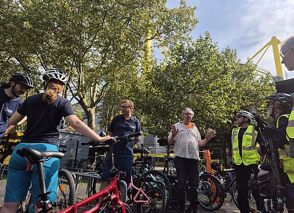Menschen in Areal der Radwache, im Hintergrund das Stadion. 